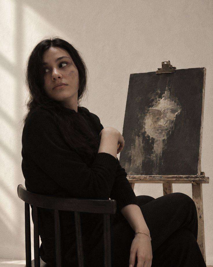 Ala Hesam seated beside one of her paintings on an easel